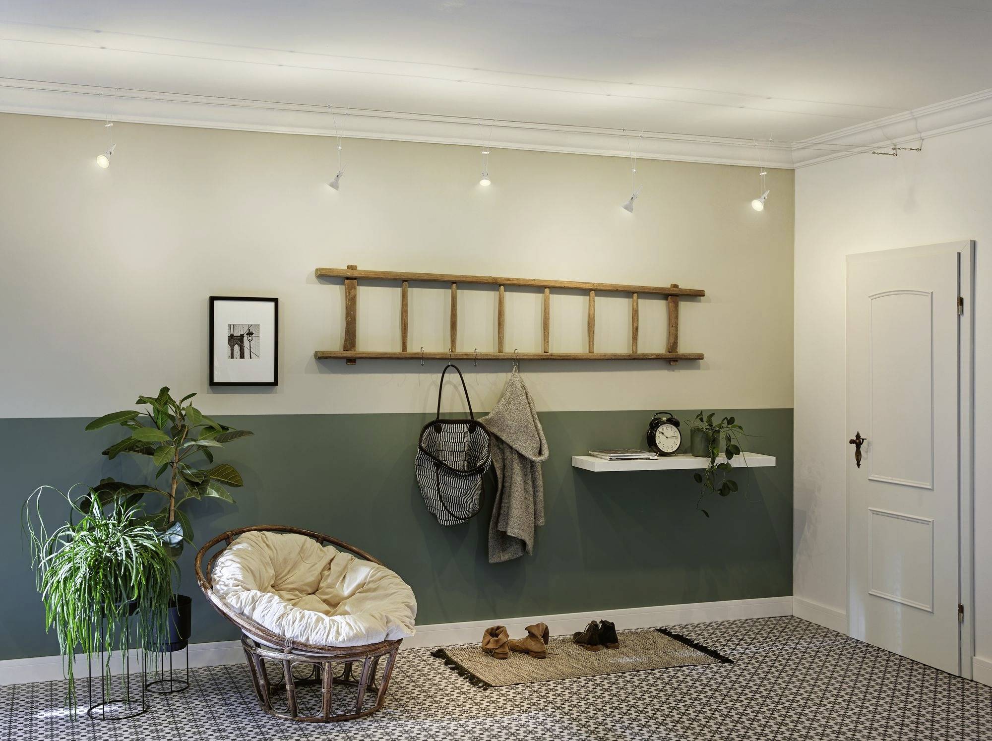 Przytulny salon z fotelem, roślinami, regałem drabinowym na ścianie, dywanem i oświetleniem; harmonijna, relaksacyjna atmosfera.