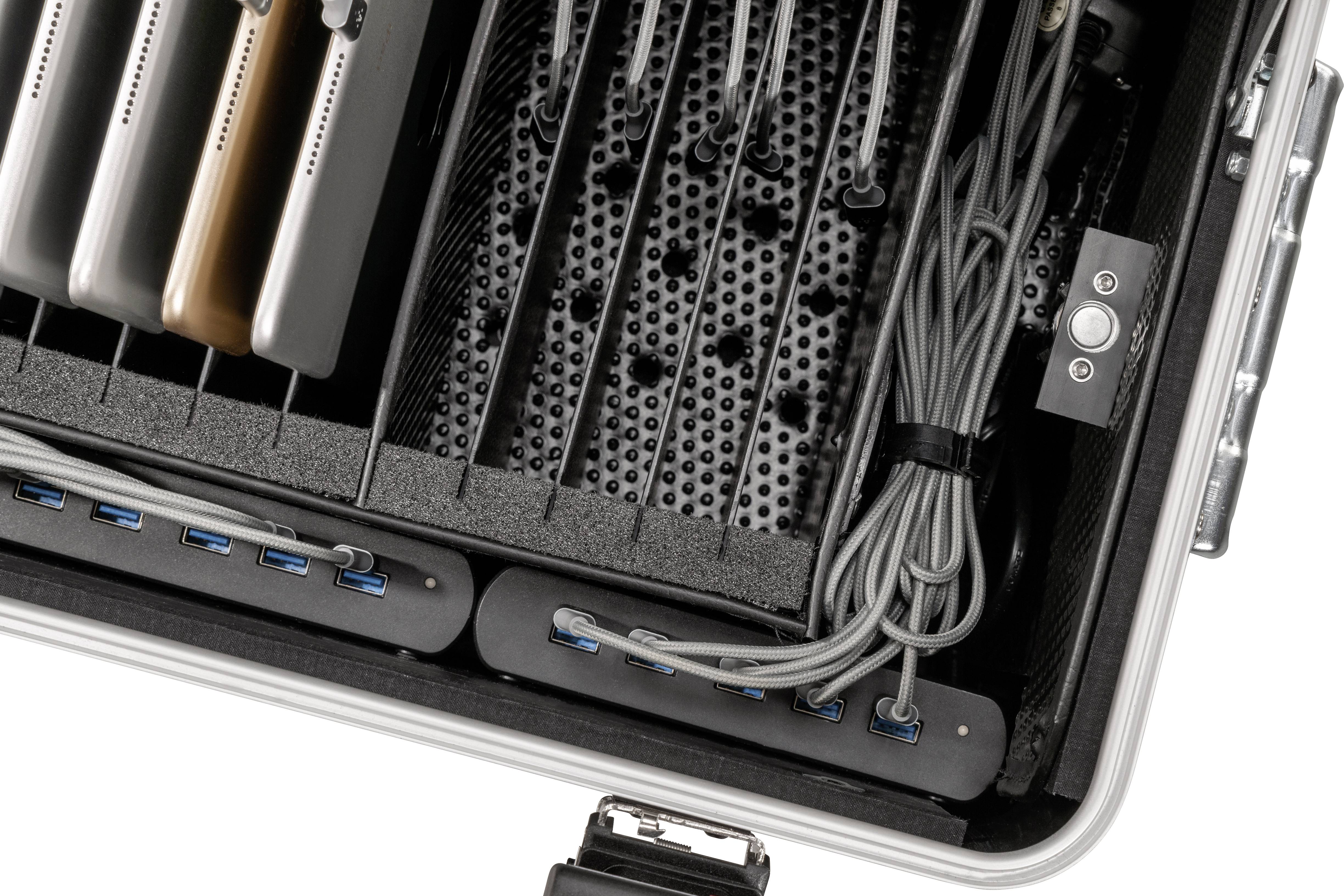 'Otwarty kufer z wieloma laptopami, kablami i portami USB, służący do organizacji i ładowania urządzeń.'