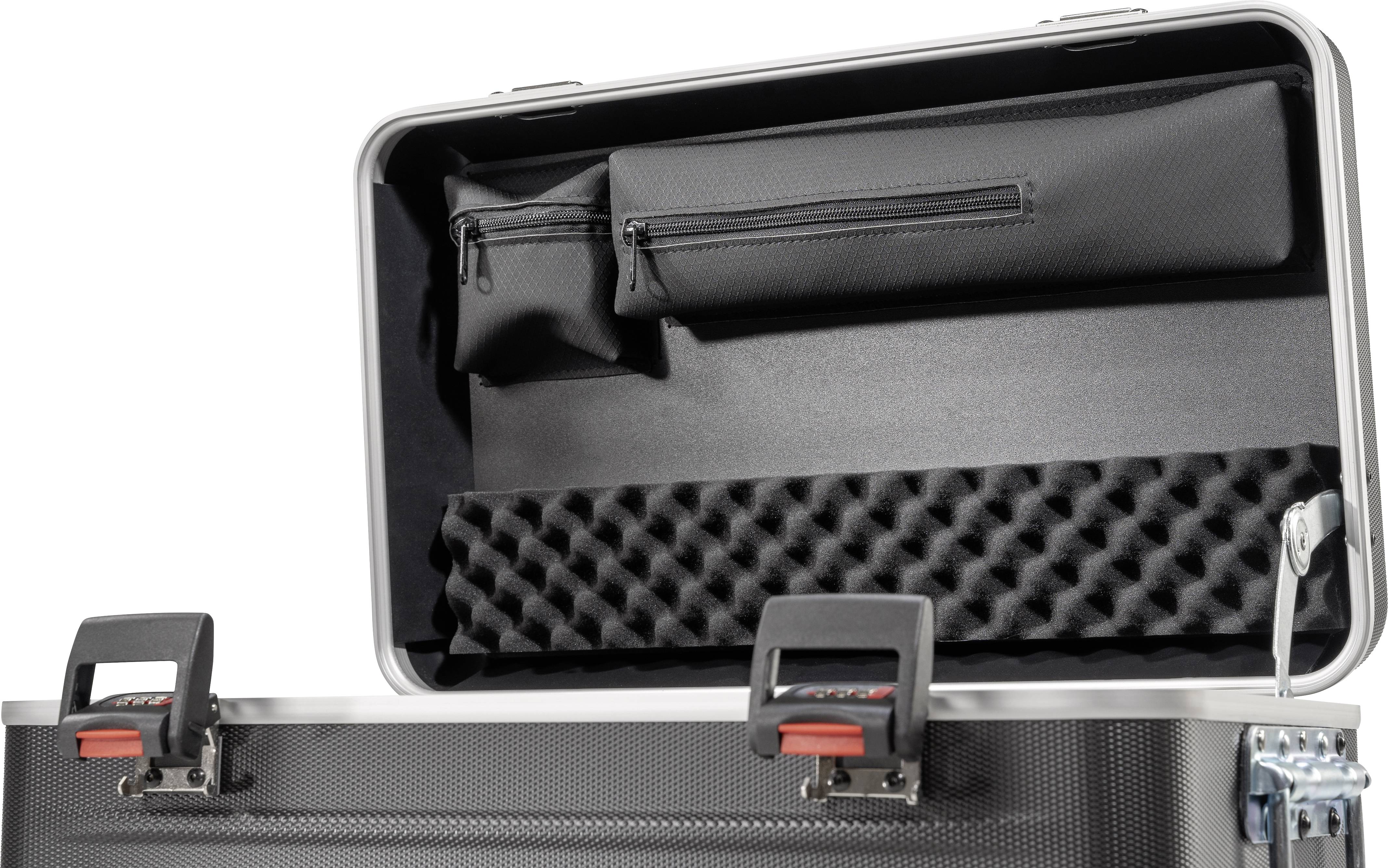 Otwarty czarny kufer z wyściółką piankową i dwiema zamykanymi na zamek błyskawiczny kieszenią w pokrywie. Kłódki walizki są otwarte.