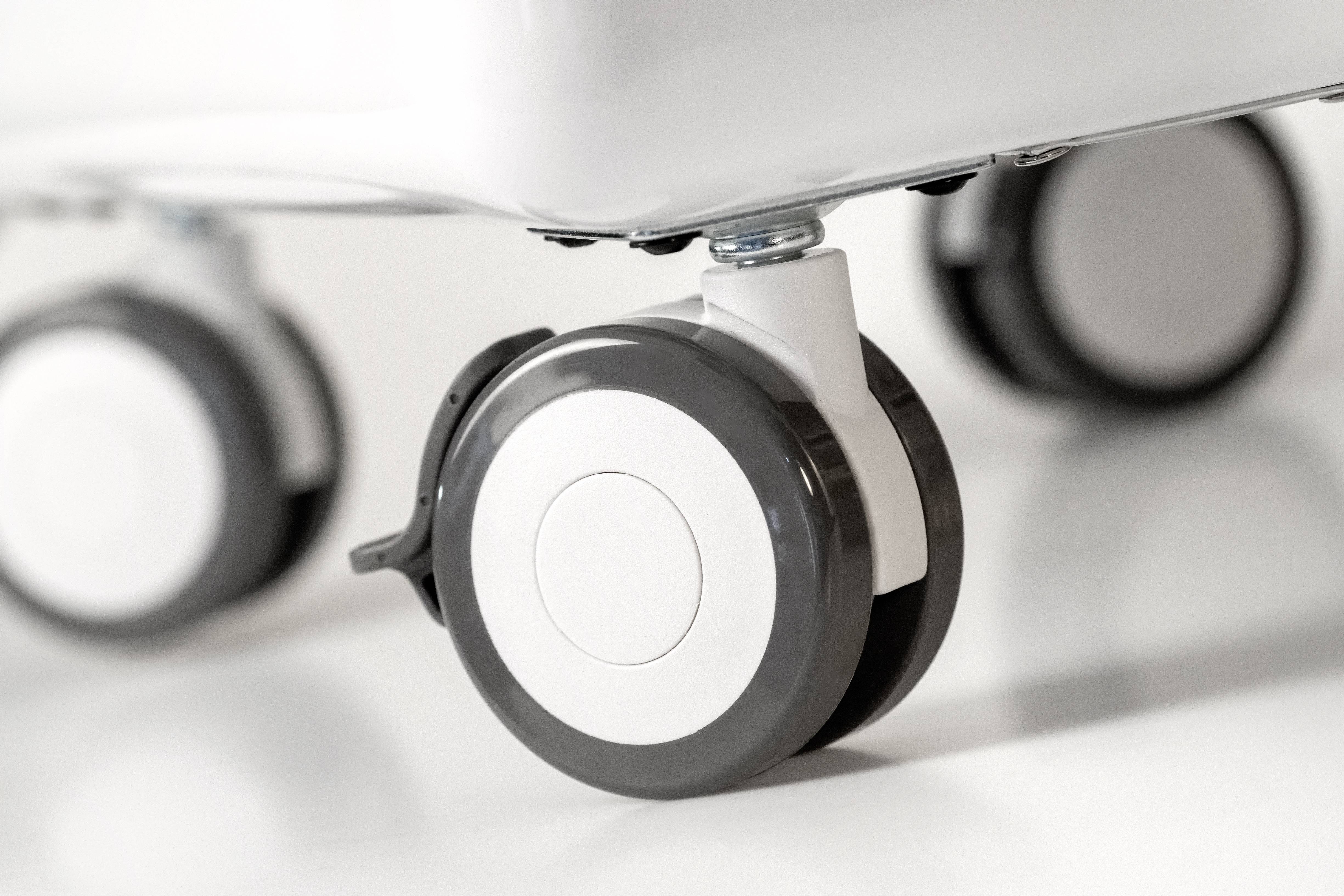 Zbliżenie czterech czarno-białych kółek od krzesła na białej podłodze. Kółka są obrotowe i wyglądają na nowoczesne.