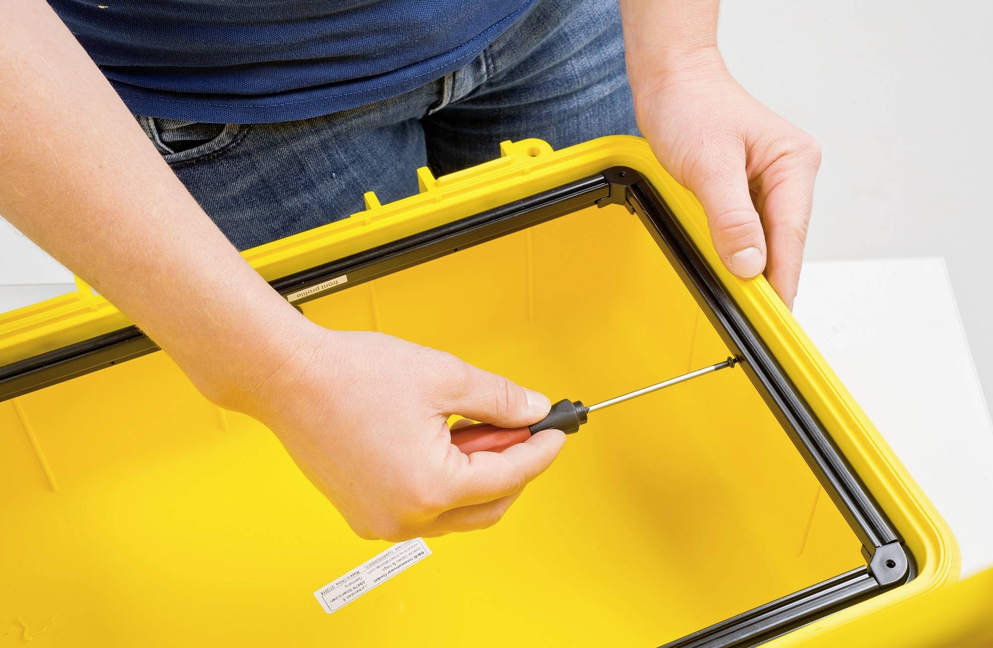 Osoba przykręca ramę żółtego pudełka wkrętakiem.