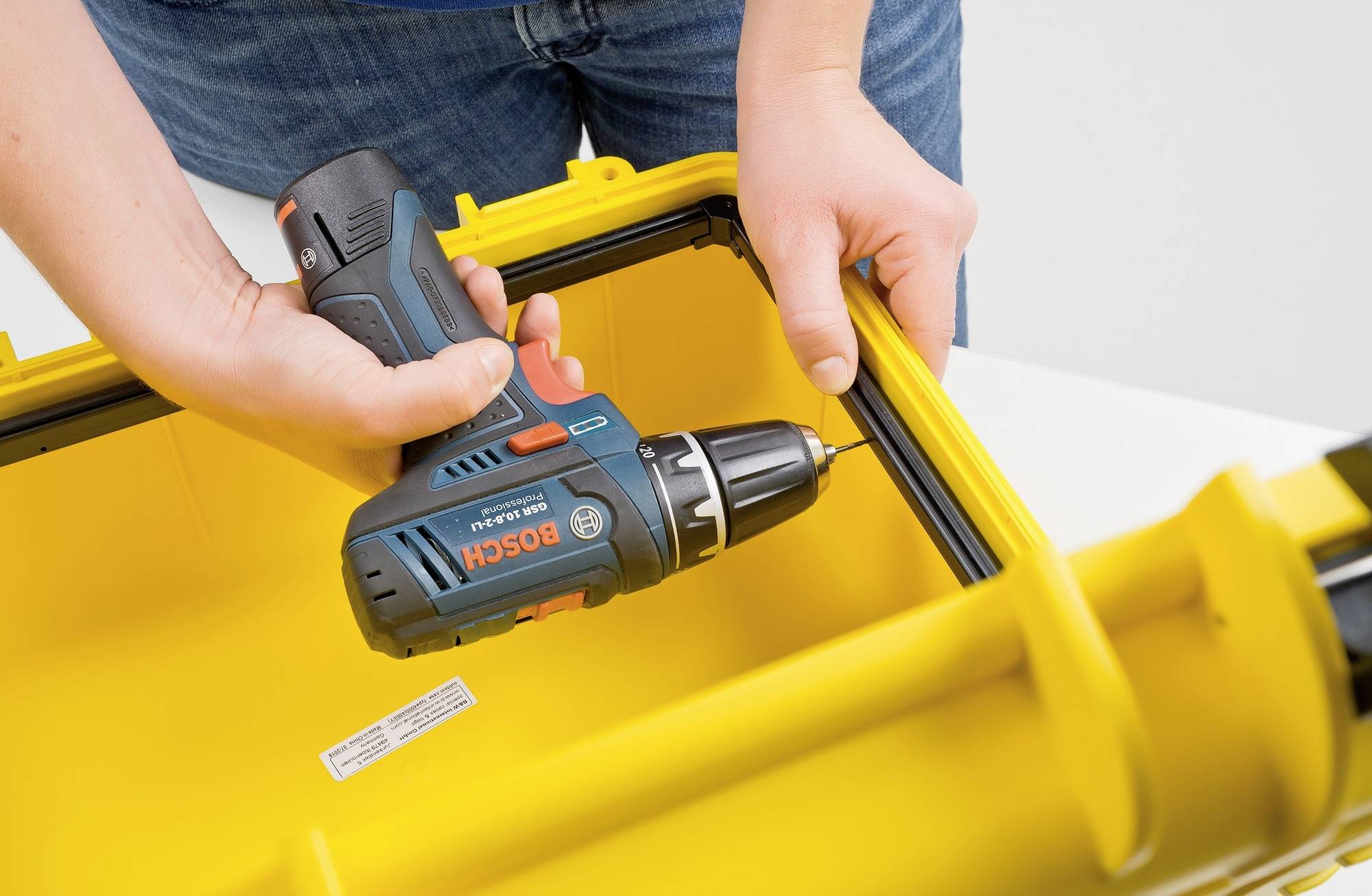 Jedna osoba trzyma wkrętak akumulatorowy i przykręca śrubę w żółtym pojemniku z tworzywa sztucznego.