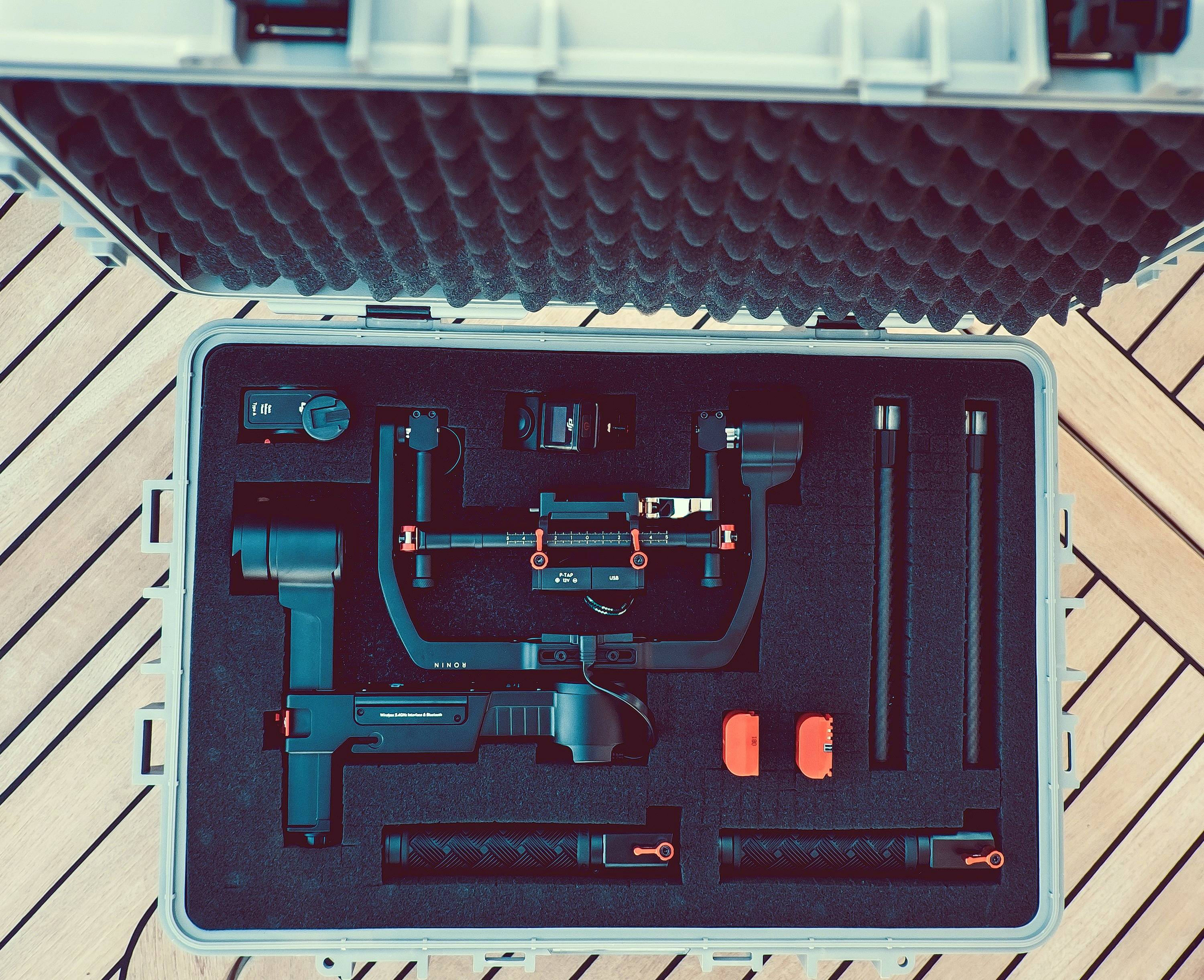 Otwarty kufer pokazuje elektroniczny system stabilizacji wraz z uchwytami i akcesoriami. Kufer leży na drewnianym pokładzie.