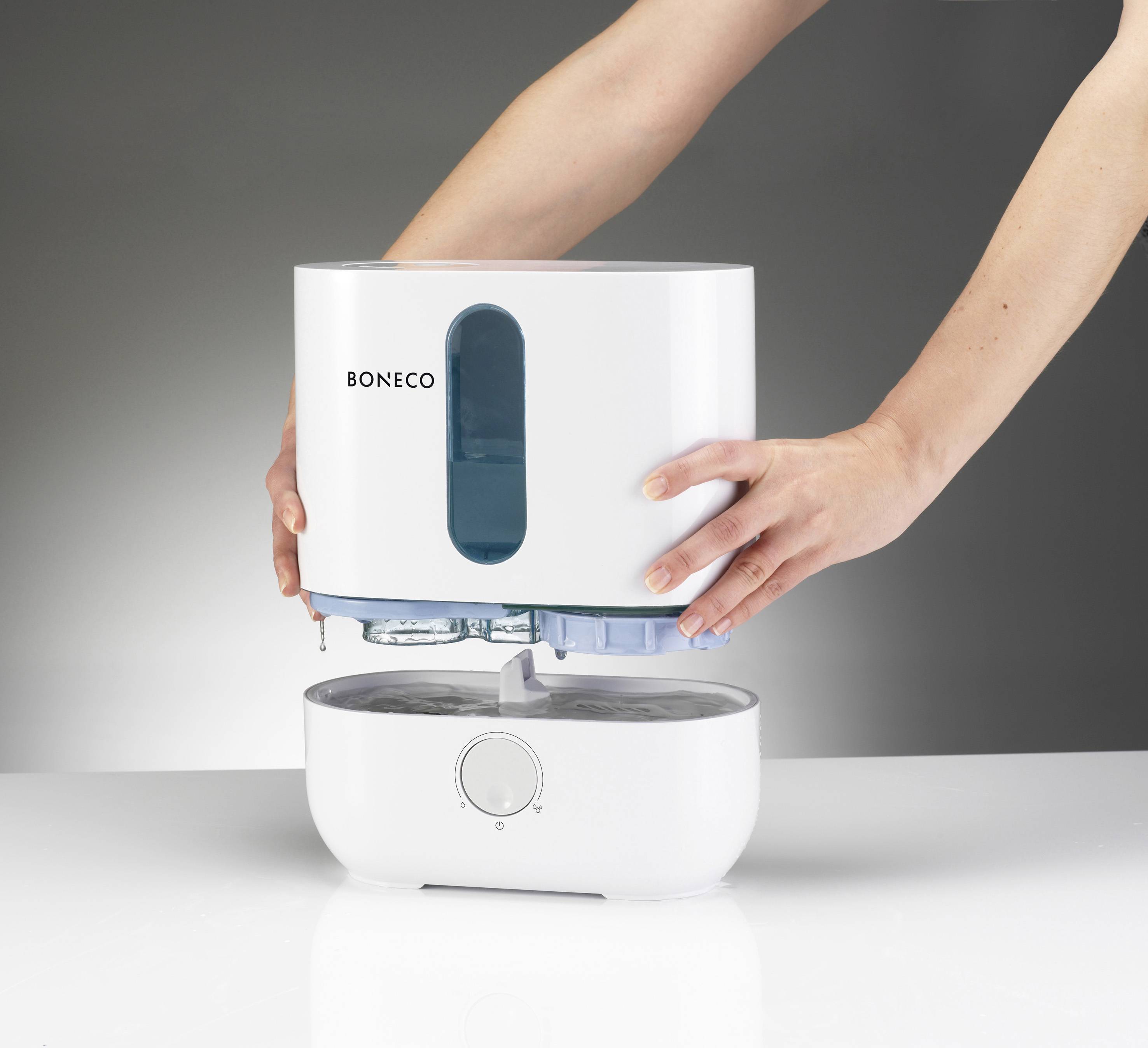 Osoba ustawia zbiornik wody nawilżacza powietrza na jego podstawie. Nawilżacz jest marki Boneco.