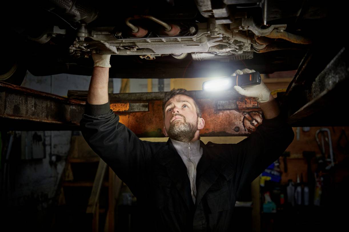 Mechanik naprawia samochód, leżąc pod pojazdem i świecąc latarką w komorę silnika w warsztacie samochodowym.