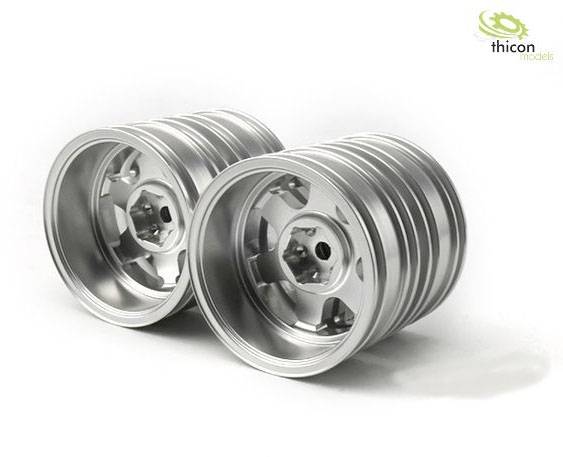 Dwie srebrne felgi z precyzyjnym wzorem leżą obok siebie na białym tle.