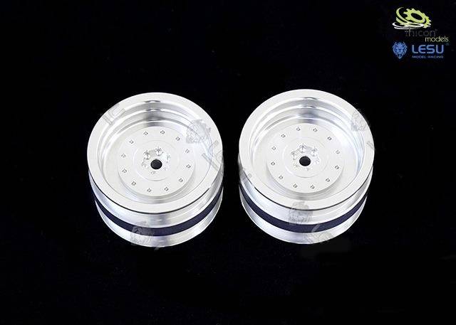 Dwa srebrne metalowe koła z dokładnie opracowanymi felgami na czarnym tle, prawdopodobnie elementy modelu.