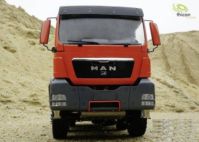Czerwona ciężarówka stoi na tle wzgórz piaskowych. Na przedniej części pojazdu widnieje napis 'MAN'. Logo Thicon Modelle znajduje się w górnym prawym rogu.
