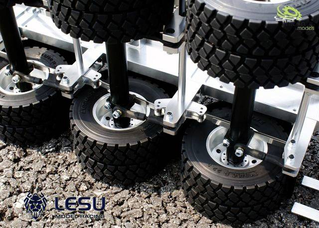 Koła modeli ciężarówek stoją w dwóch rzędach na asfalcie. Logo producenta 'Lesu Model Racing' widoczne w lewym dolnym rogu.