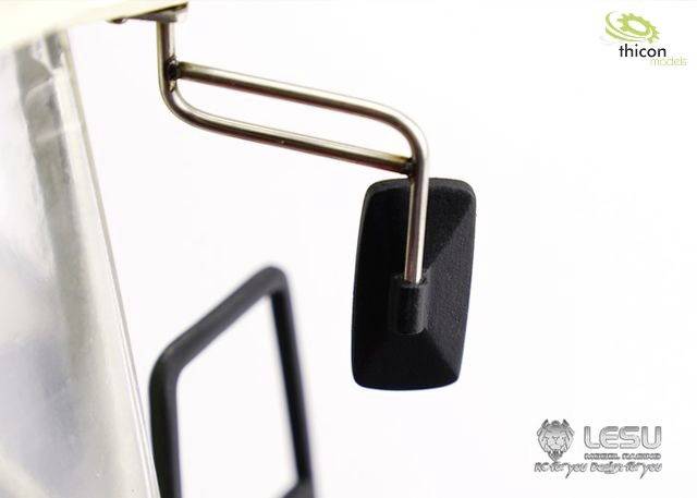 Zbliżenie czarnego lusterka bocznego zamontowanego na modelu pojazdu za pomocą dwóch metalowych ramion w kształcie litery L. W górnym prawym rogu widoczne jest logo.