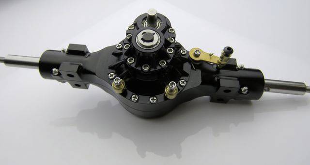 Czarna, skomplikowana część mechaniczna z kołami zębatymi i śrubami, używana w budowie maszyn lub technice samochodowej.