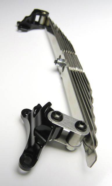 Metalowa belka z elementami mocującymi i śrubami na białym tle, prawdopodobnie część komponentu maszyny lub pojazdu.