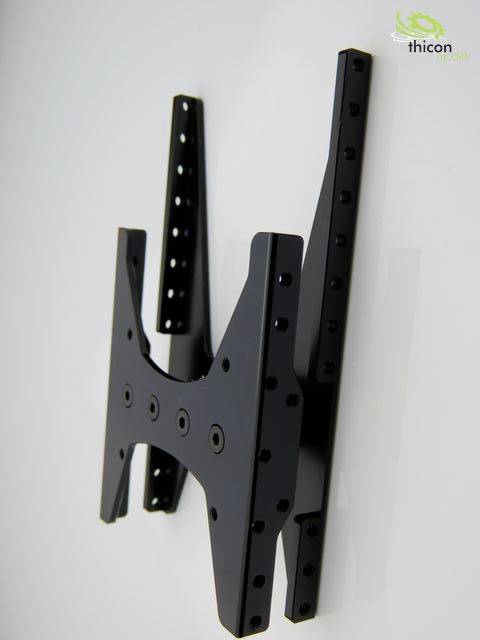 Czarna ścienna podstawa telewizyjna na białej ścianie, składająca się z dwóch pionowych szyn z wieloma otworami na śruby.