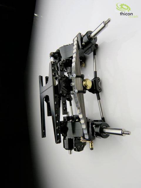 Mechaniczny zespół złożony z metalowych elementów i kół zębatych zamontowany na gładkiej ścianie. W górnym prawym rogu logo 'thicon models'.