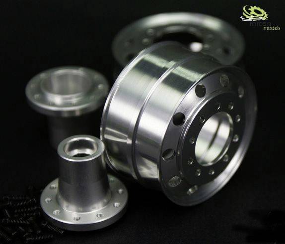 Srebrne metalowe części do modelarstwa, w tym duży adapter piasty koła i inne komponenty, na czarnym tle.