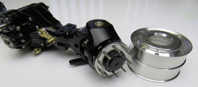 'Czarne mechaniczne urządzenie z kołami zębatymi obok lśniącego, srebrnego metalowego koła na białym tle.'