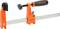 Metalowa ścisk stolarska marki Jorgensen w kolorze pomarańczowym z uchwytem z tworzywa sztucznego i szyną zaciskową do mocowania elementów obrabianych.