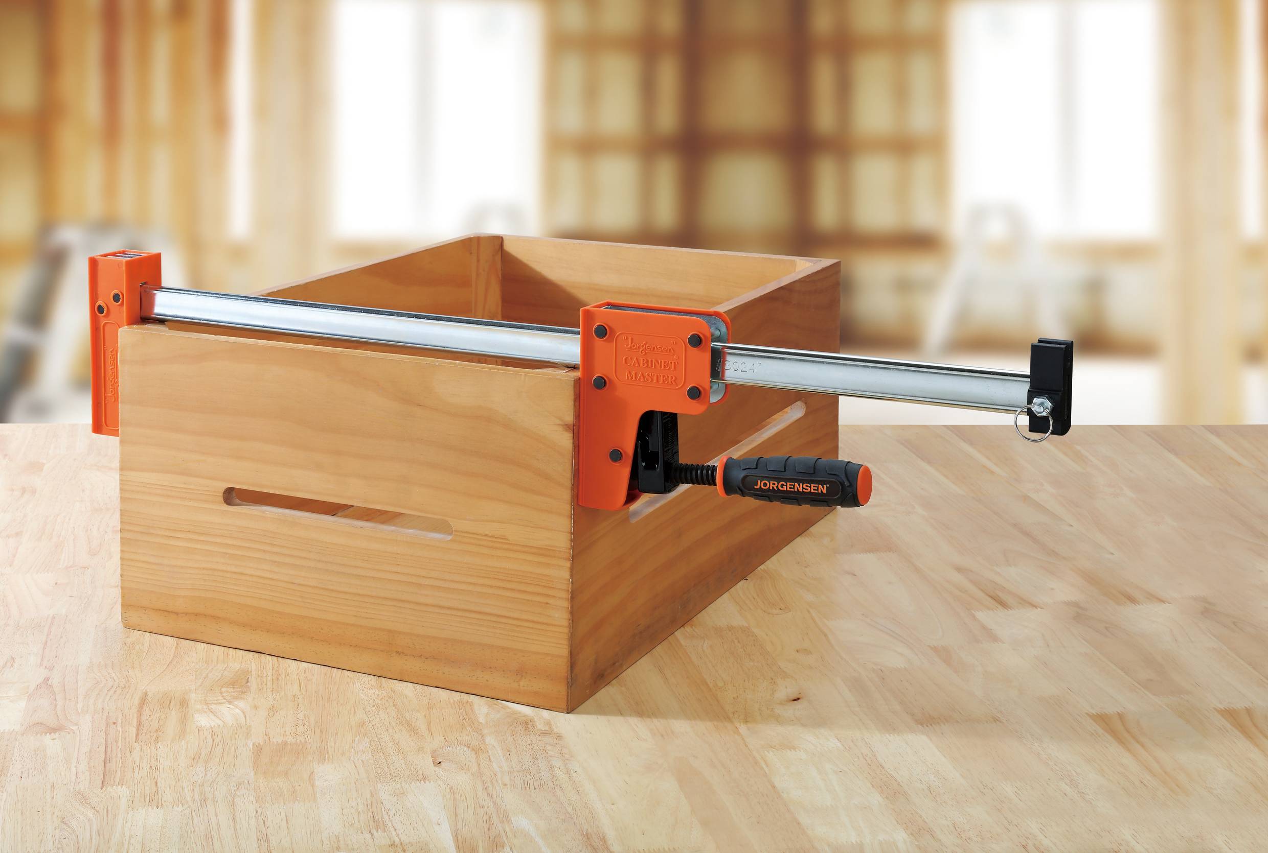 Drewniana skrzynia jest mocowana dużym zaciskiem do stołu, w tle rozmazane środowisko warsztatu.