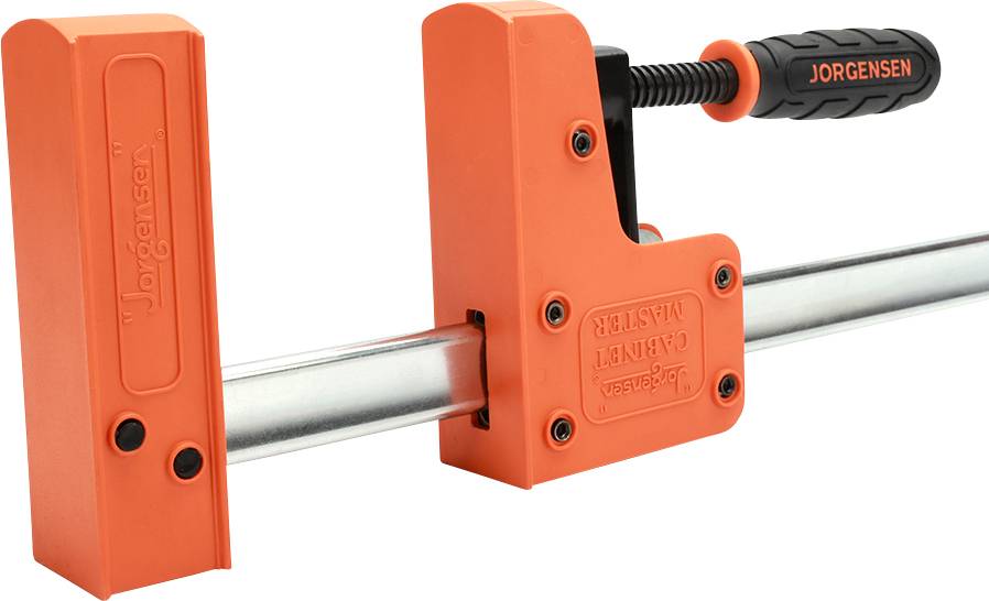Pomarańczowy zacisk marki Jorgensen zamocowany na metalowym pręcie, używany do mocowania materiałów podczas prac stolarskich lub metalowych.