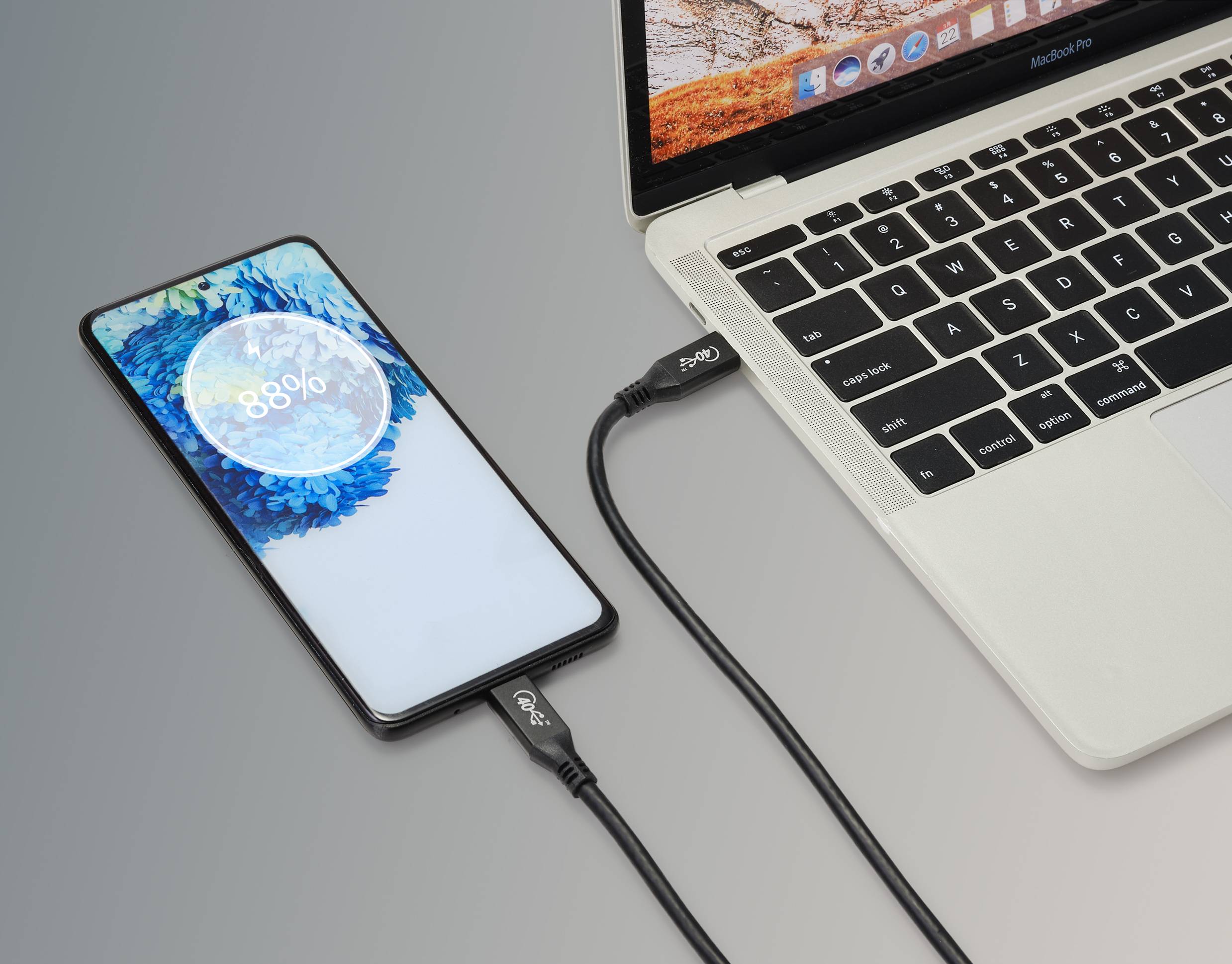 Smartfonładowany z laptopa przez kabel USB, wyświetlacz pokazuje 88% naładowania. Ekran prezentuje animację ładowania. Laptop z otwartym ekranem.