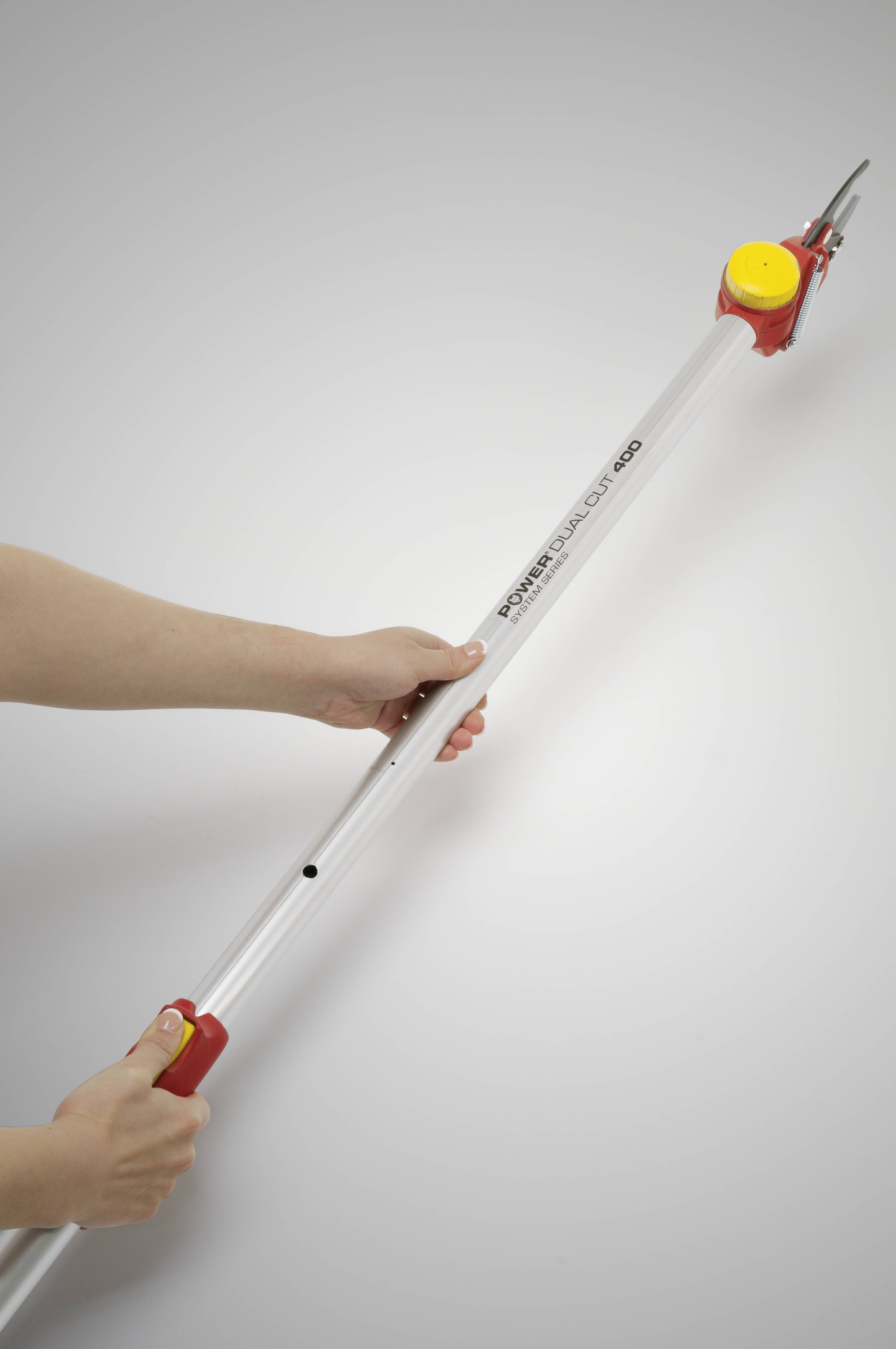 'Dwie ręce trzymają długie, srebrne teleskopowe nożyce ogrodowe z żółtym mechanizmem obrotowym i czerwoną głowicą, na szarym tle.'