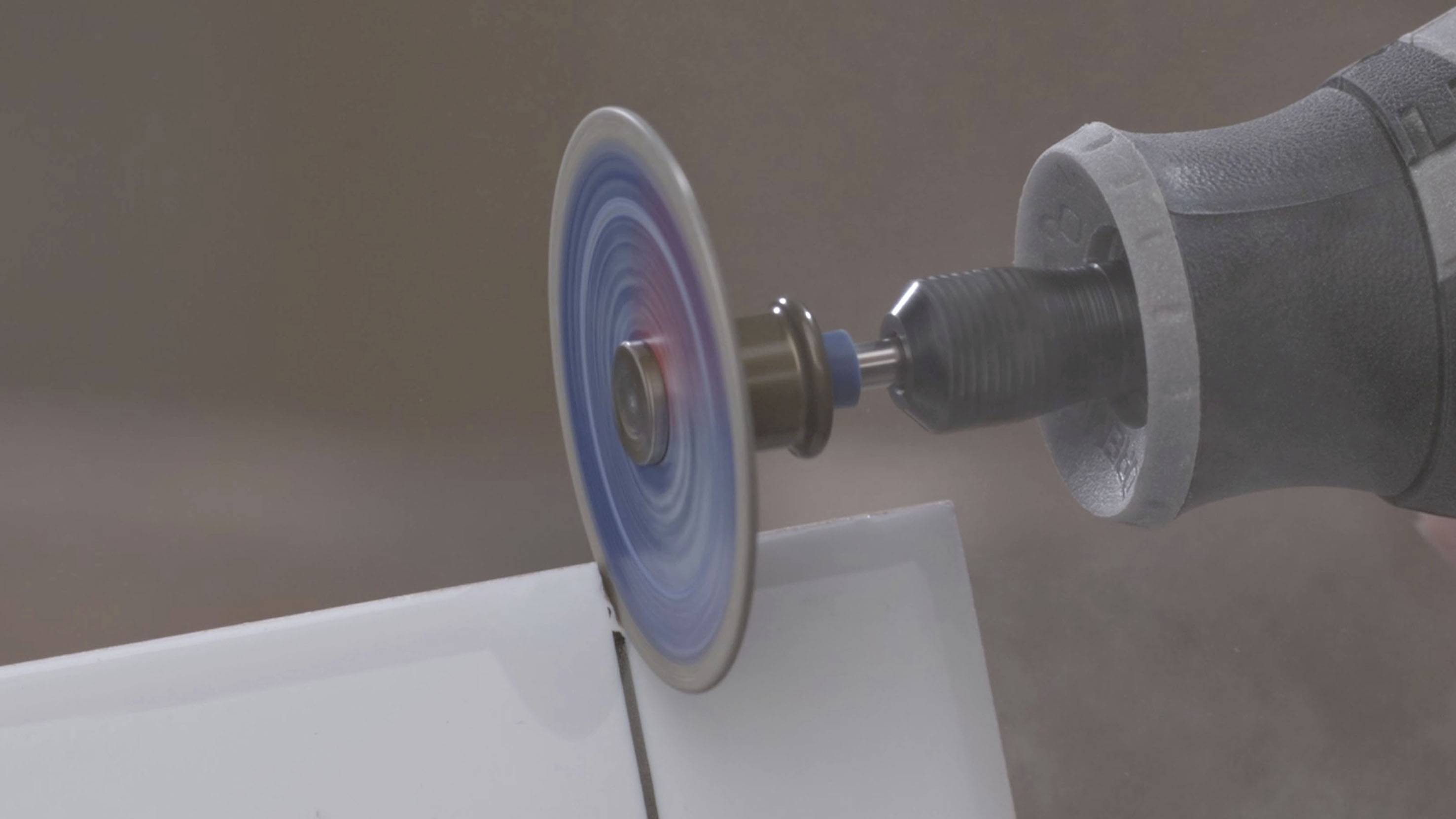 Zbliżenie obracającej się tarczy tnącej, która przecina białe tworzywo. Podczas procesu cięcia powstaje pył.