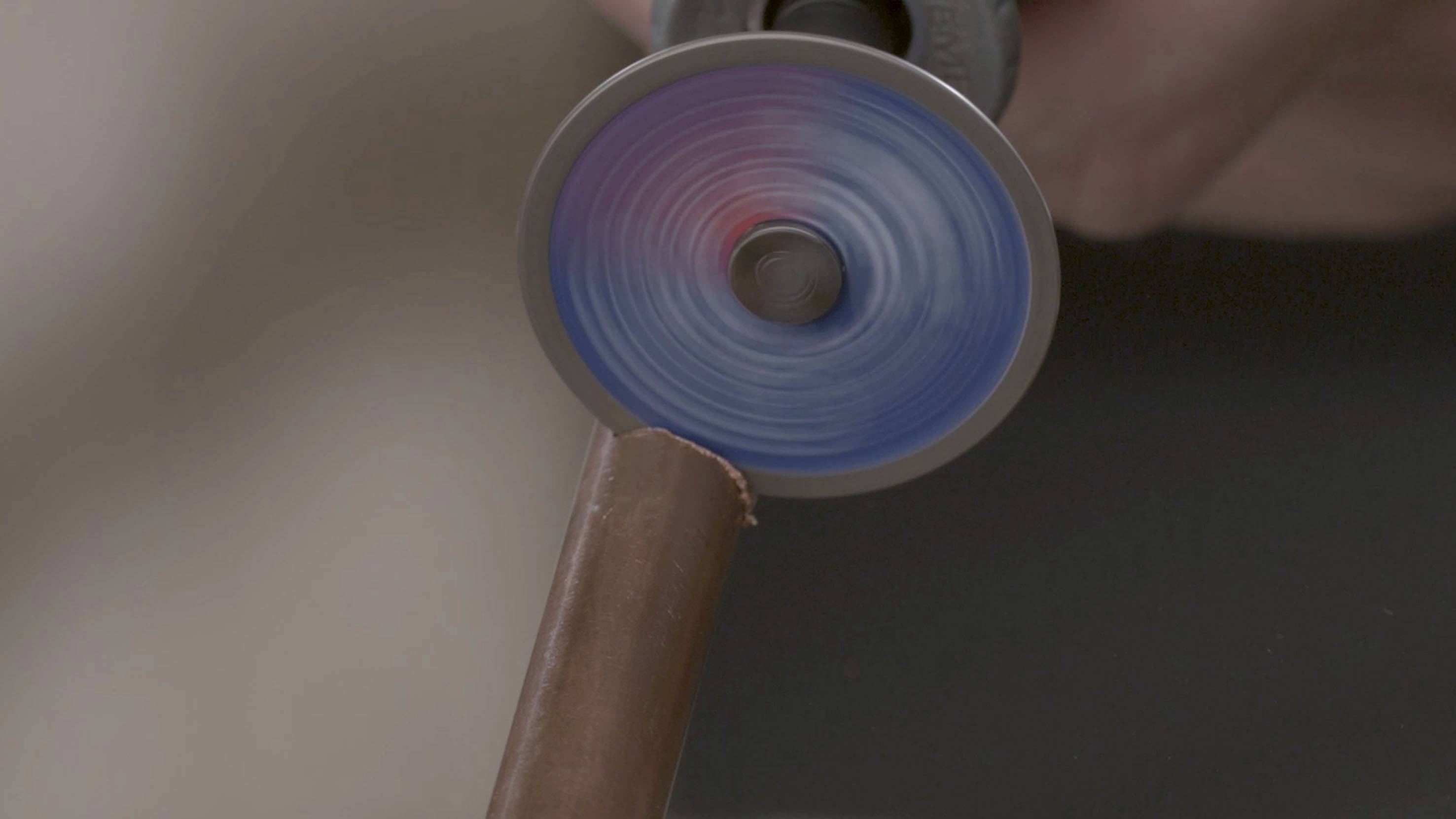 Obracająca się tarcza tnąca precyzyjnie przecina brązową rurę metalową. Dynamiczny ruch i koncentracja na cięciu.