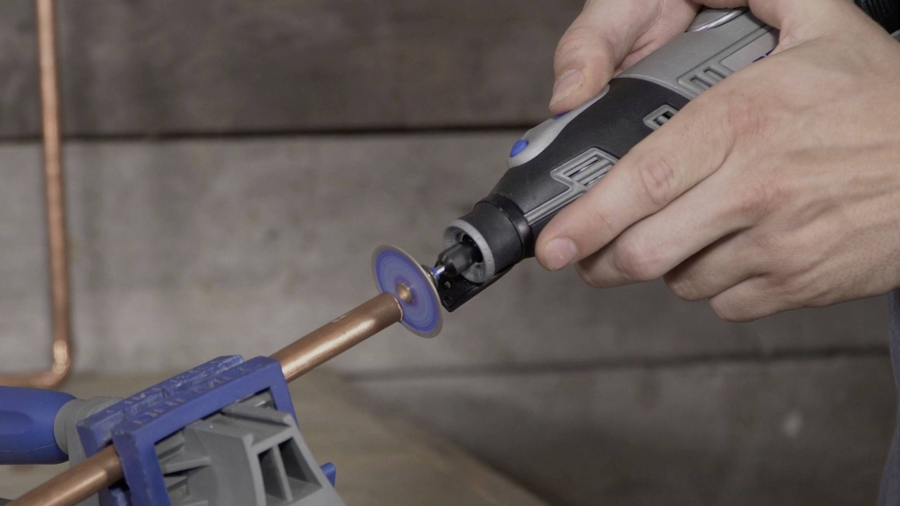 Osoba przecina rurę miedzianą obrotowym narzędziem zamocowaną w imadle.