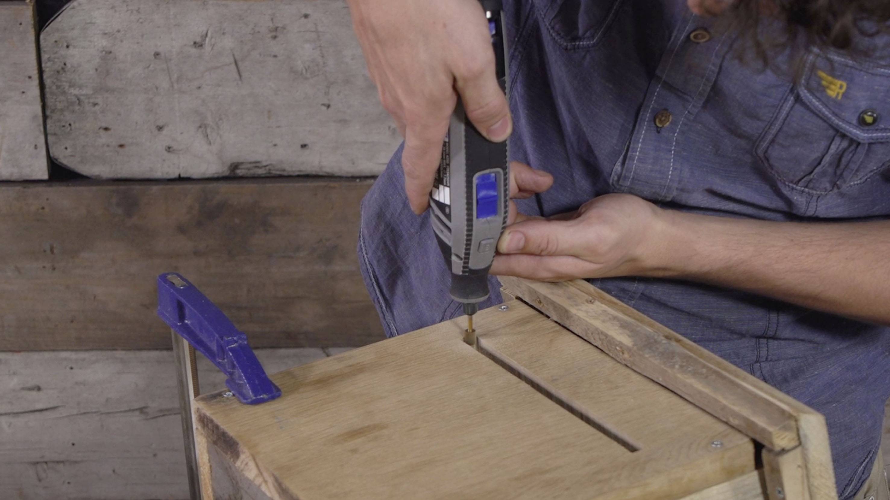 Osoba używa wielofunkcyjnego narzędzia do obróbki kawałka drewna. W tle widać drewnianą boazerię.