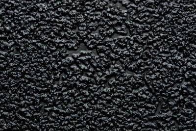 Szorstka czarna powierzchnia teksturowa z nieregularnymi wypukłościami i zagłębieniami.