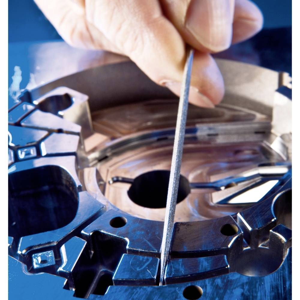 Ręka piluje metalowe koło zębate pilnikiem, podkreślając precyzję i rzemiosło.