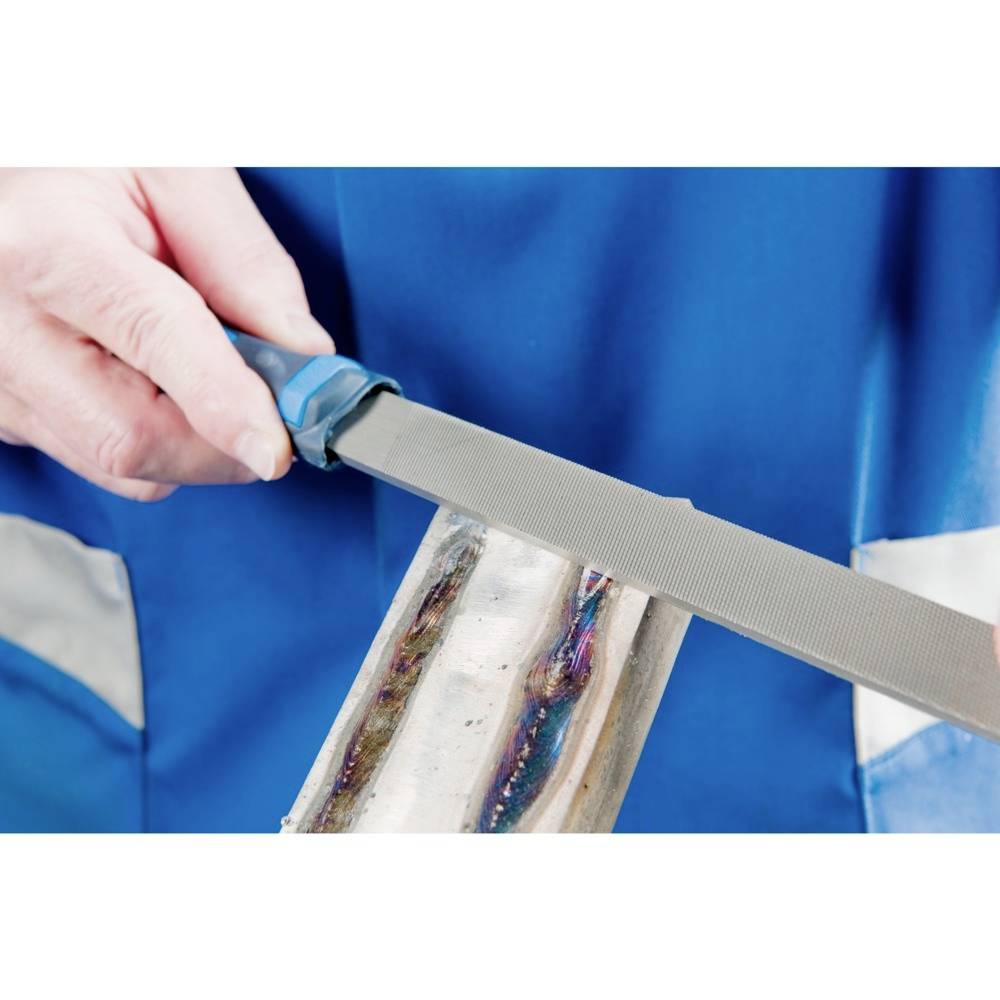 Osoba pilnikuje metalową rurę pilnikiem. Nosi niebieski fartuch. Koncentruje się na ruchu ręki i pilnika.