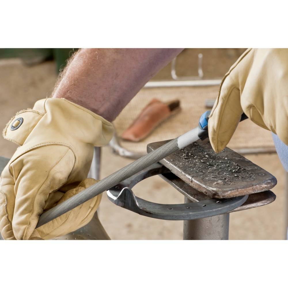 Osoba w rękawicach ochronnych piluje metal na kowadle w warsztacie.