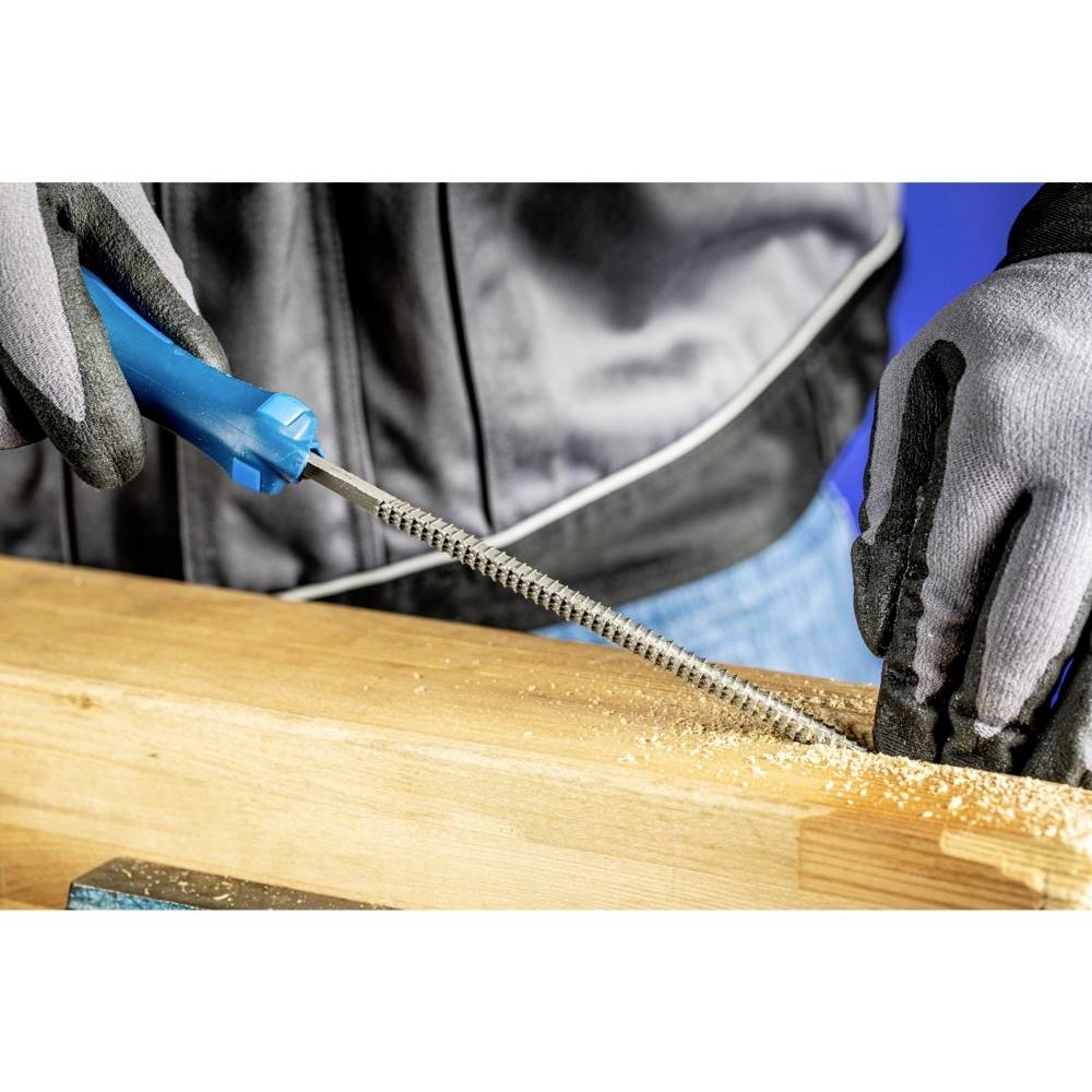 Osoba pilnikuje kawałek drewna, przy czym widoczne są wióry. Osoba ma na rękach rękawice i używa niebieskiego pilnika.