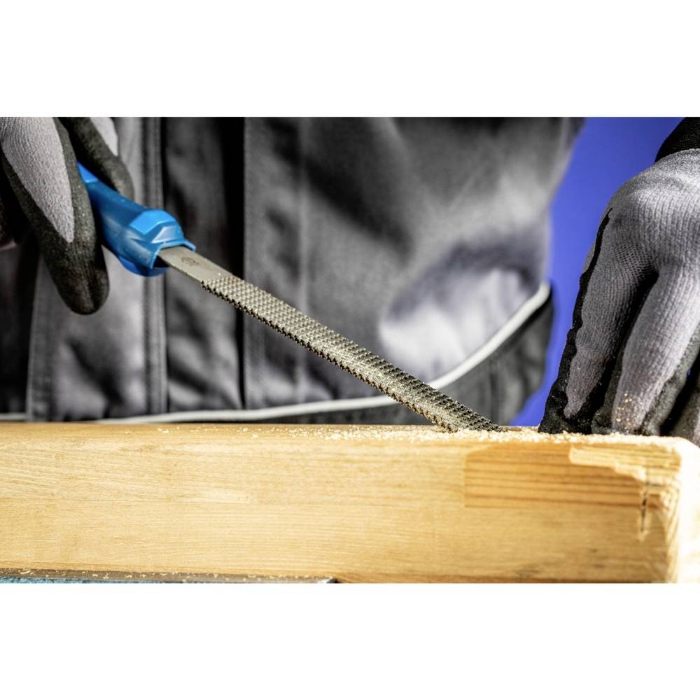 Osoba piluje drewno niebieską pilnikiem, ubrana w czarne rękawiczki i szarą kurtkę.