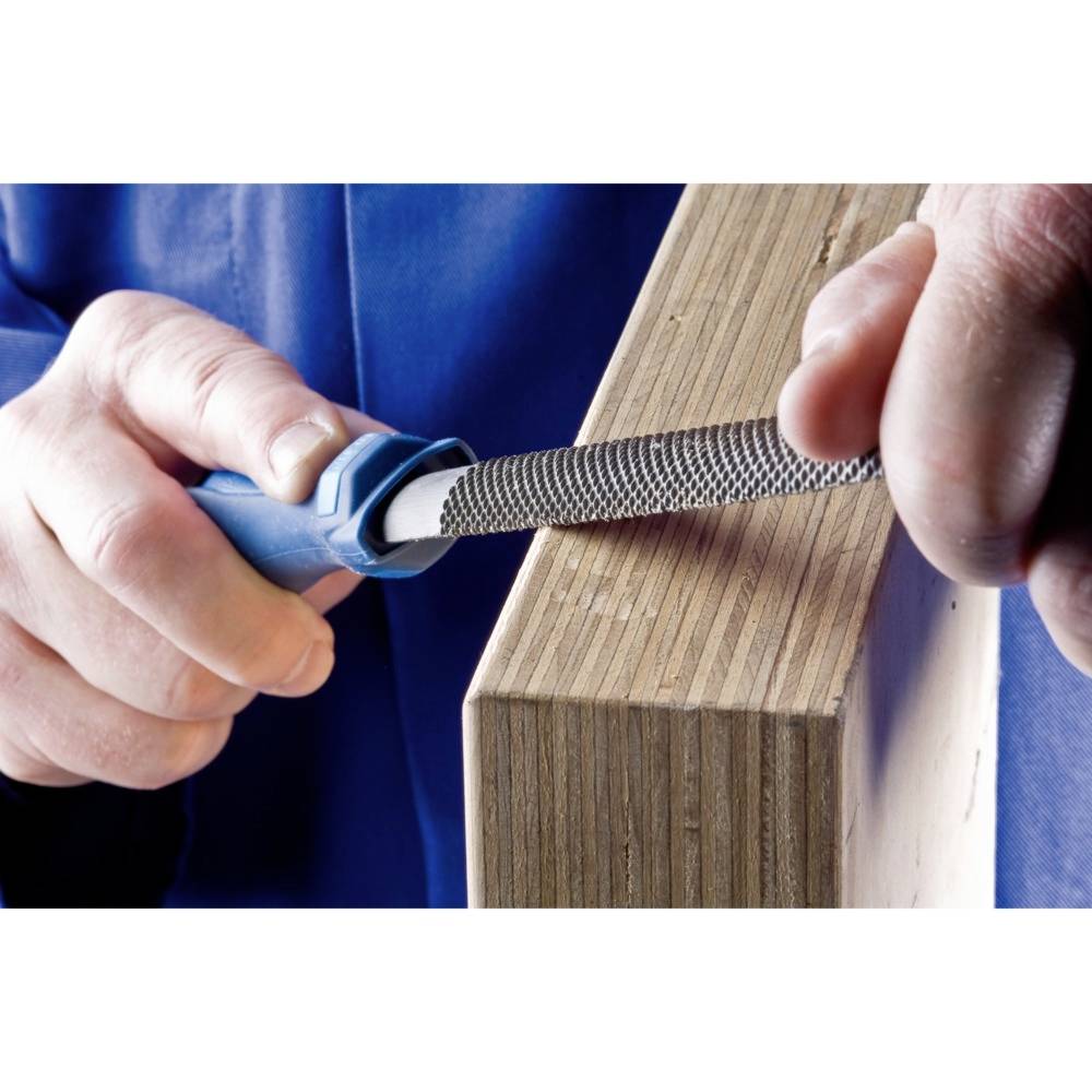 Osoba pilnikiem wygładza róg drewnianej deski. Zbliżenie ukazuje użycie narzędzia do obróbki powierzchni drewna.