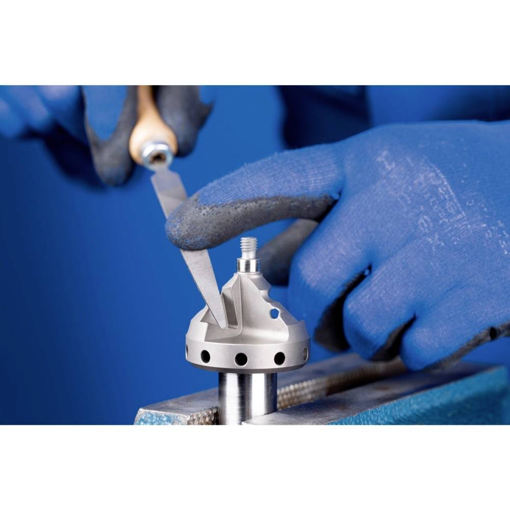 Dwie dłonie w niebieskich rękawiczkach pracują narzędziem przy metalowym elemencie zamocowanym w uchwycie.