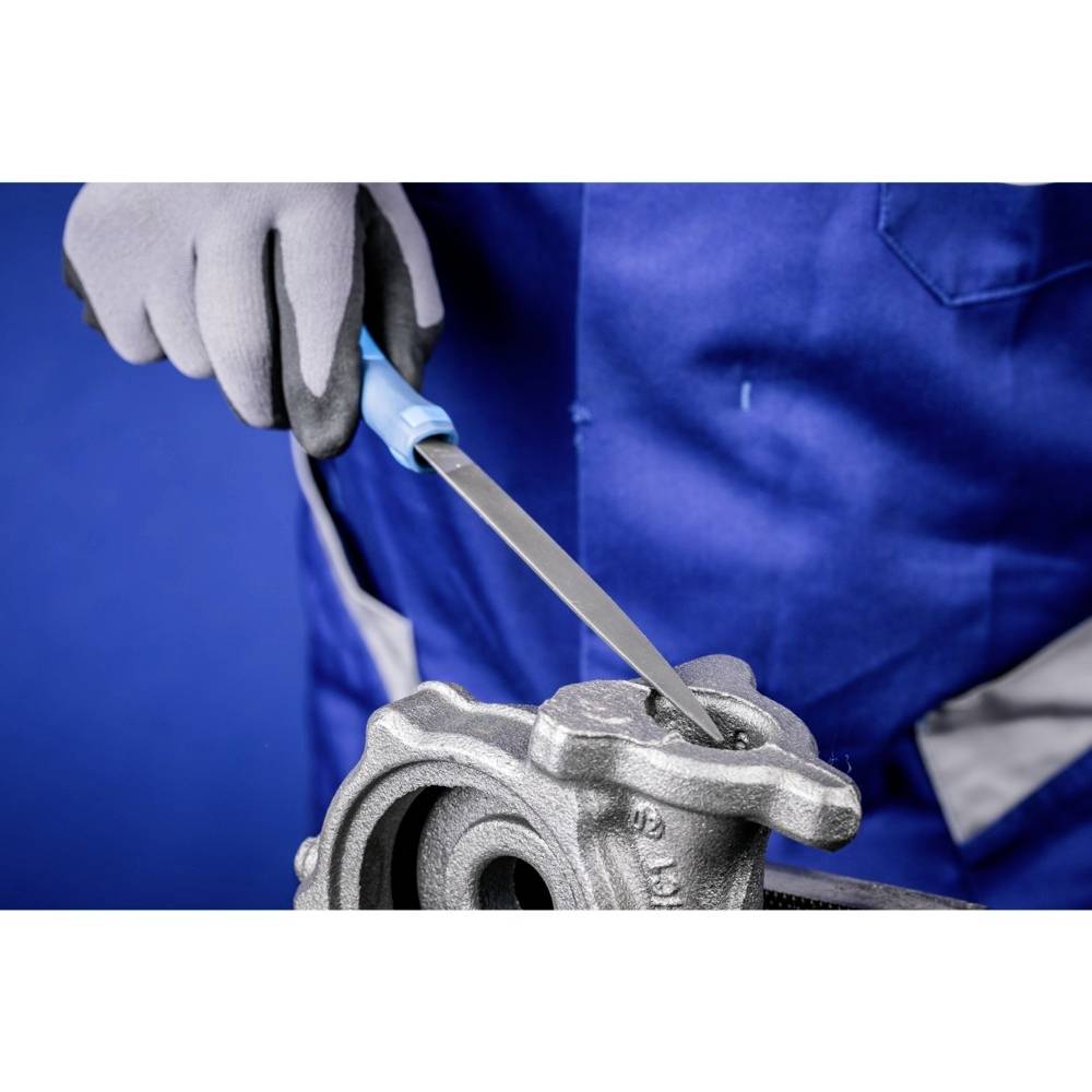 Rzemieślnik w niebieskim ubraniu roboczym piluje element metalowy za pomocą pilnika metalowego.