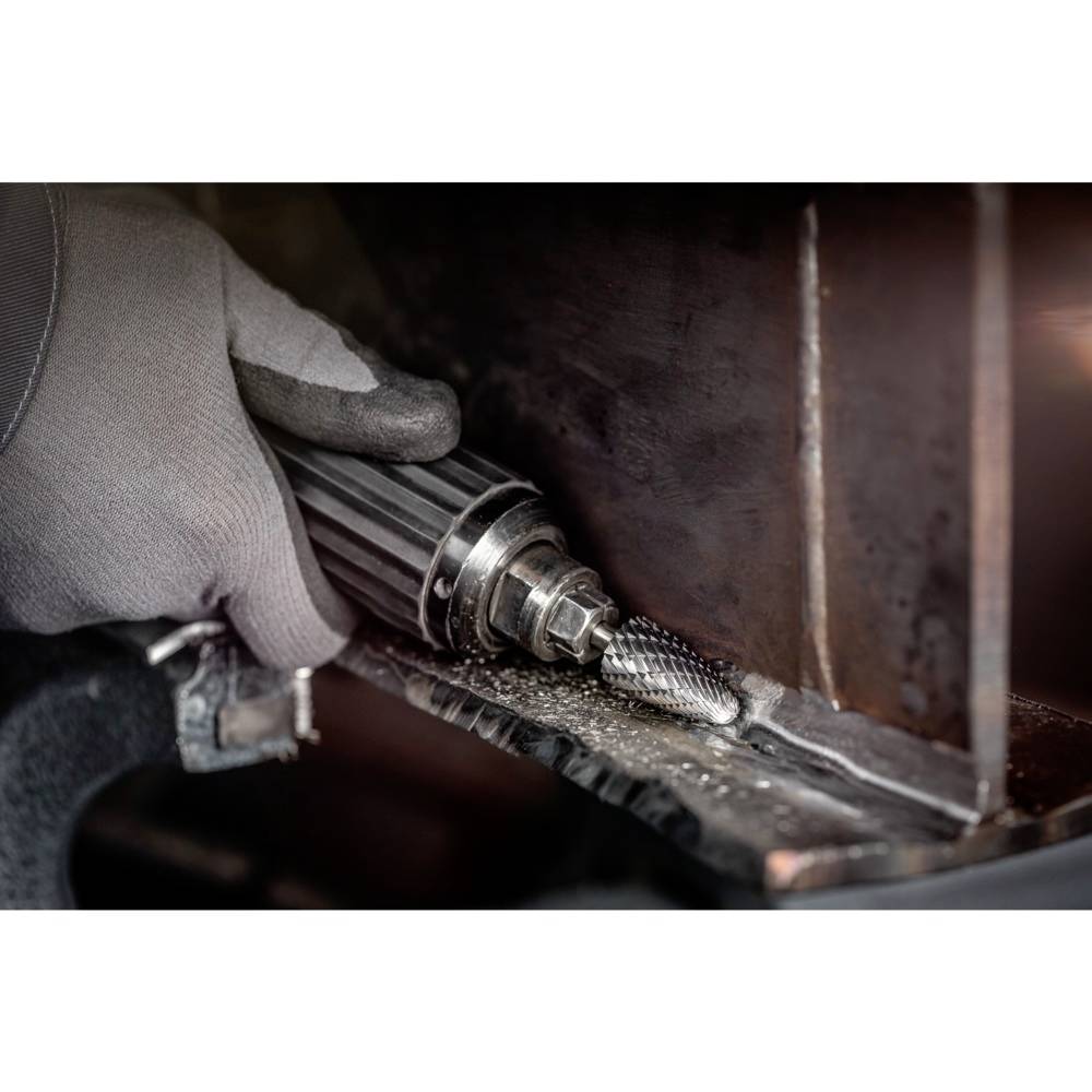 Jedna ręka trzyma obracające się narzędzie szlifujące metal. Iskry lecą na ciemnym tle. Nacisk na precyzję i rzemiosło.