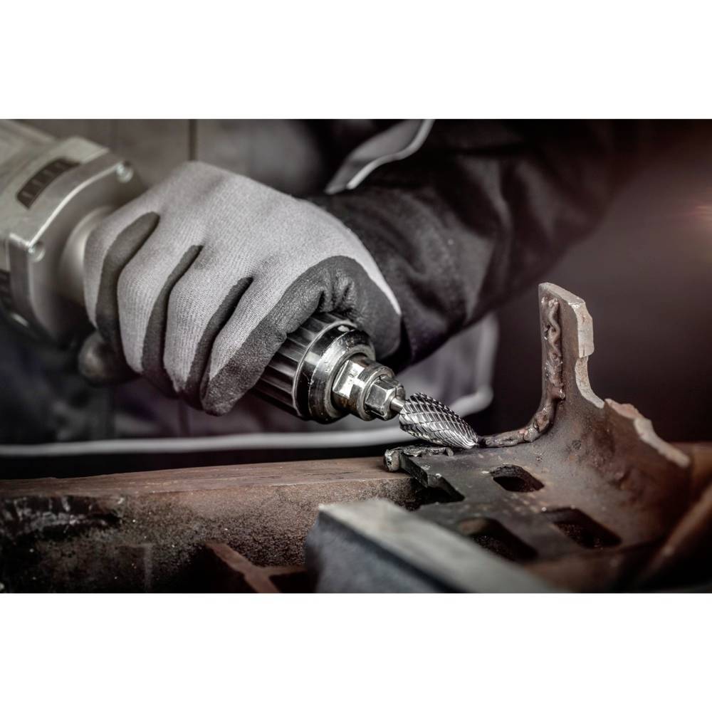 Osoba w rękawicach roboczych używa elektronarzędzia do obróbki metalu. Widoczne są iskry i wióry metalowe.