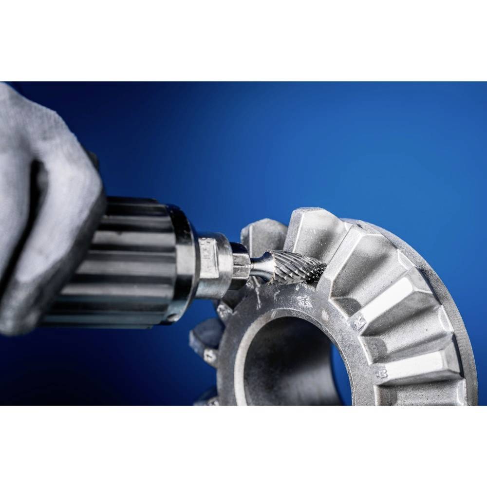 Dłoń w rękawicach obrabia metalowe koło zębate obrotowym narzędziem. Tło w kolorze niebieskim.