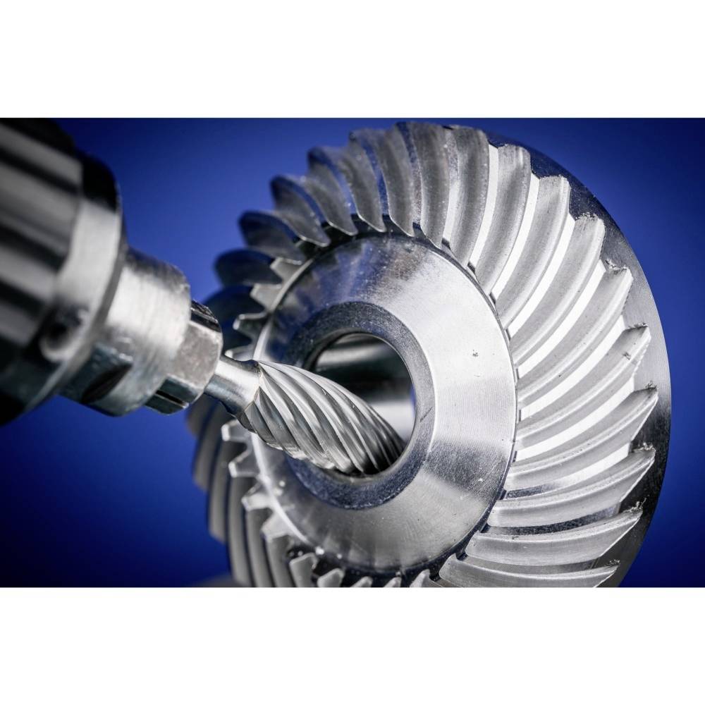 Frezarka obrabia duże metalowe koło zębate na niebieskim tle, prezentując szczegółową pracę i precyzję w obróbce maszynowej.