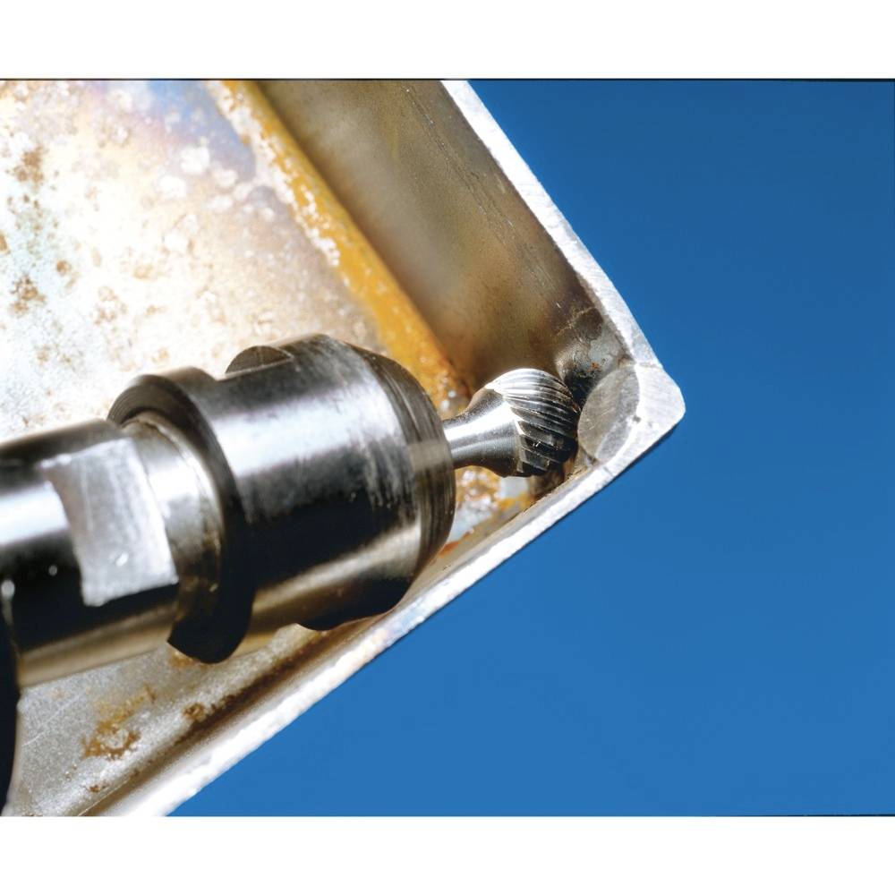 Frezarka precyzyjnie obrabia ostry brzeg kawałka metalu. Powierzchnia wykazuje ślady rdzy, a tło jest niebieskie.