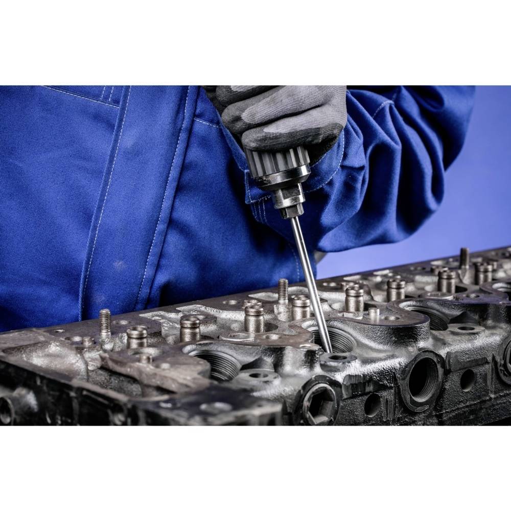 Mechanik w niebieskim kombinezonie roboczym używa narzędzia do obróbki głowicy cylindra w warunkach warsztatowych.