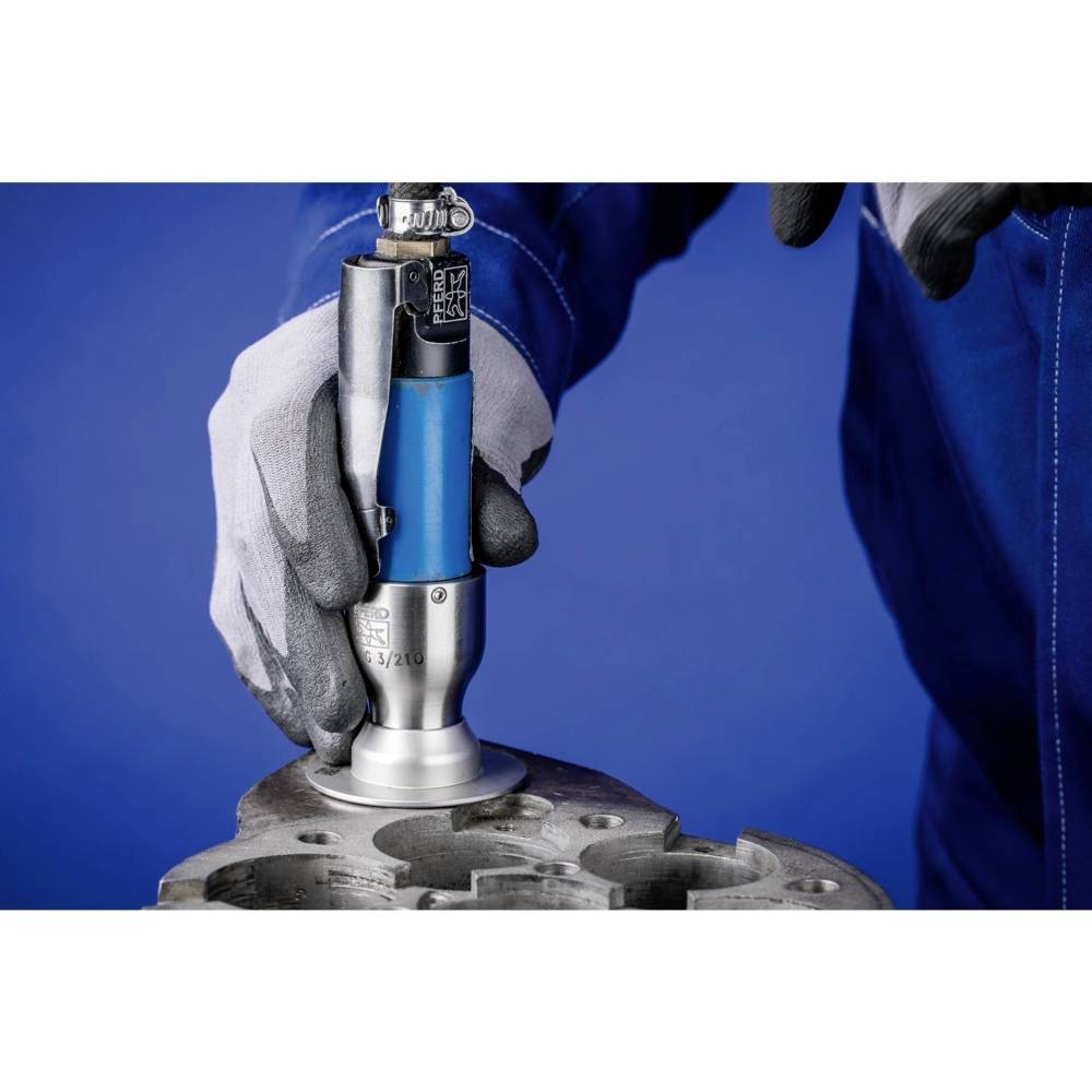 Osoba ubrana w niebieskie ubranie robocze i szare rękawice trzyma narzędzie przy metalowym elemencie. Narzędzie jest częściowo niebieskie.