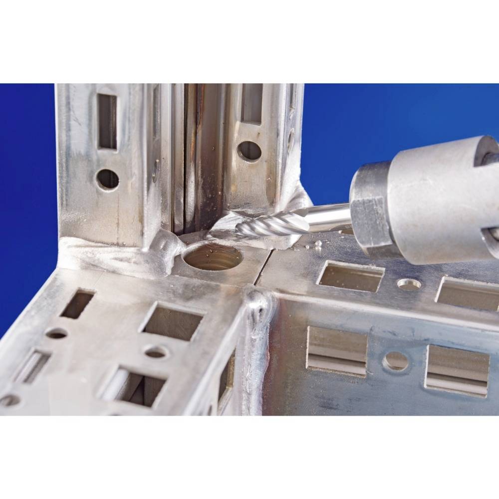 Wiertło przebija część metalową w przemysłowym otoczeniu. Tło jest niebieskie.