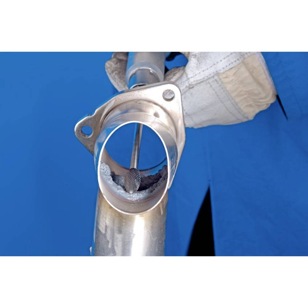 Osoba w niebieskim ubraniu roboczym obsługuje wnętrze metalowej rury narzędziem. Praca techniczna w centrum uwagi.