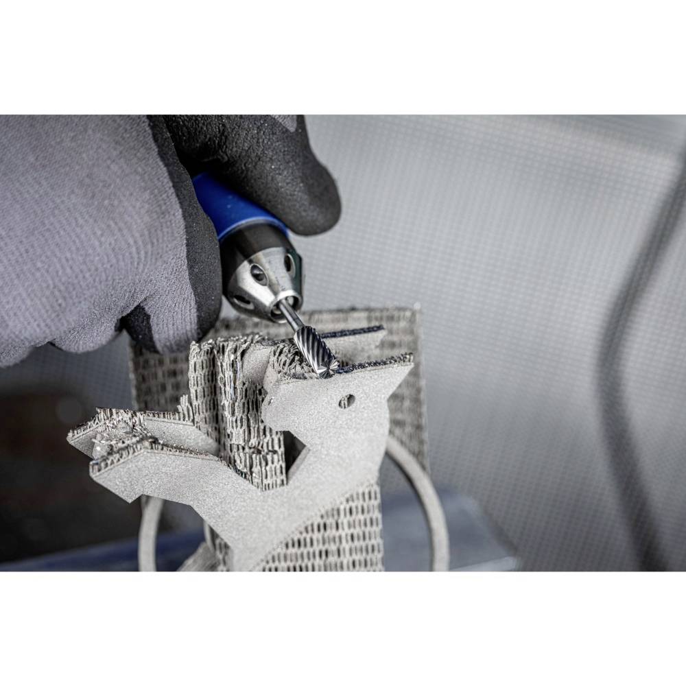 Zbliżenie dłoni w rękawicach roboczych obrabiających wiertłem metalową rzeźbę wydrukowaną w technologii 3D.