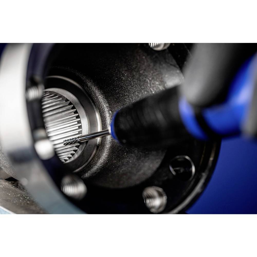 Zbliżenie przemysłowej wiertarki wykonującej otwór w metalowym kole zębatym. Widoczne są śruby i części maszyny.