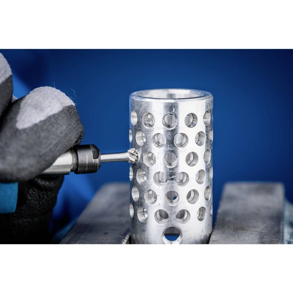 Dłoń w rękawicy trzyma obracające się narzędzie, które wierci otwory w metalowym cylindrze na niebieskim tle.